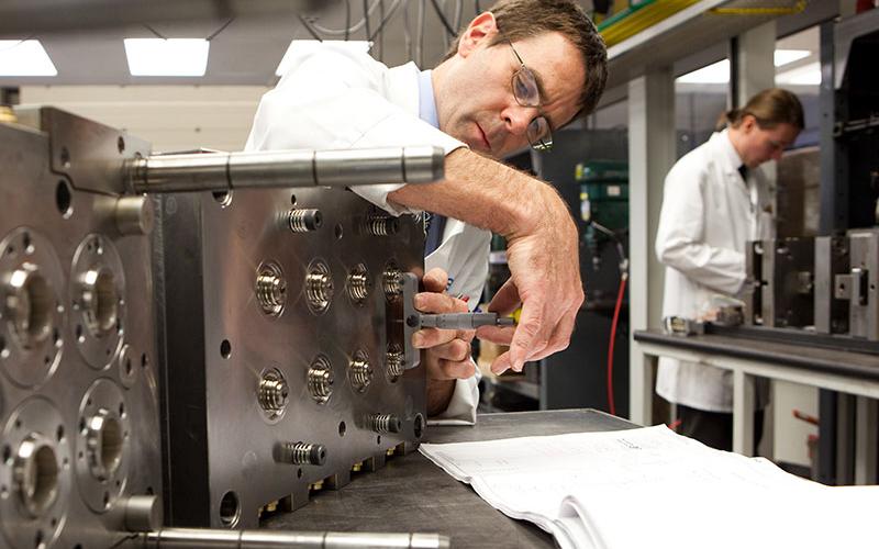 Gentleman in lab coat constructing part of a machine.