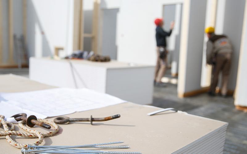 close up of metal tools on a table with a blurred background of construction workers putting up white walls